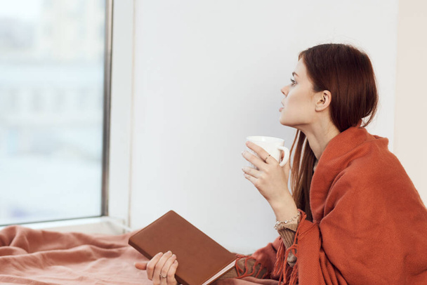 woman with a cup of drink on the windowsill reading a book rest morning - Foto, imagen