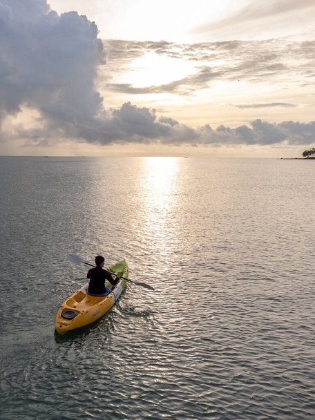 空中から見たシーカヤックの男。黄色と青のコーカサススポーツマン海岸沿いの景色の海で漕ぐカヤック. - 写真・画像