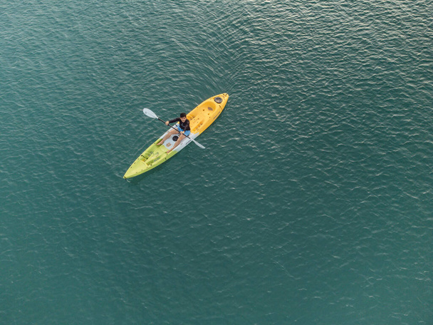 Mies merellä, Kayaker Aerial View 'sta. Valkoihoinen urheilija keltaisessa ja sinisessä kajakissa melomassa Scenic meressä pitkin rantaa. - Valokuva, kuva