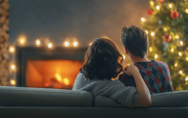 Loving couple relaxing near fireplace Christmas tree at home. - Zdjęcie, obraz