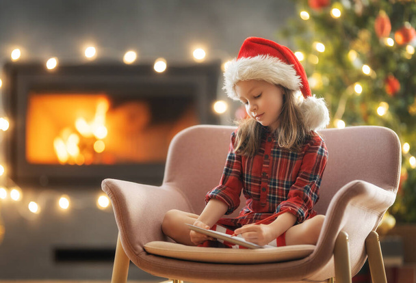 Joyeux Noël et Joyeuses Fêtes ! Petite fille mignonne écrit la lettre au Père Noël près de l'arbre à l'intérieur.  - Photo, image