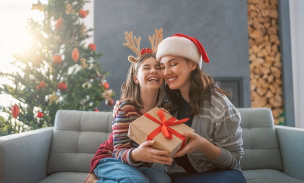 Merry Christmas and Happy Holidays. Cheerful mother and her cute daughter girl exchanging gifts. Mom and little child having fun near tree indoors. Loving family with presents in room. - Φωτογραφία, εικόνα