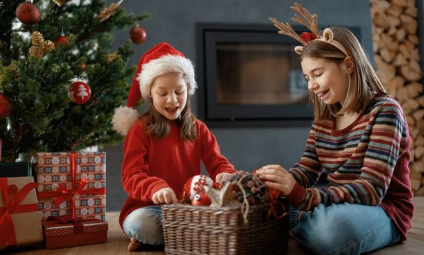 Merry Christmas and Happy Holidays. Cheerful cute childrens girls at home. Kids are having fun near tree in the morning - Φωτογραφία, εικόνα