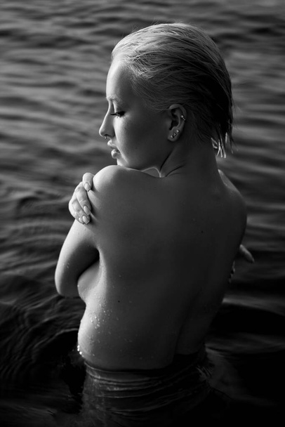 Blonde short hair woman is standing in the water on sea shore. Artistic portrait of a relaxed woman in water on shore. Black and white - Foto, Bild