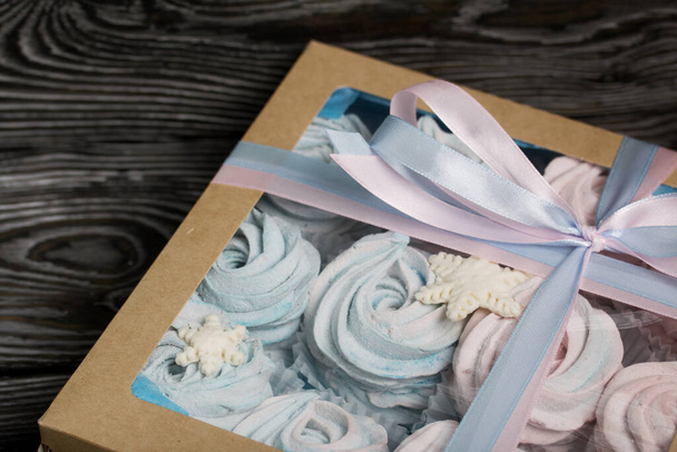 Marshmallow blue and pink. Lies in craft packaging. Decorated with mastic snowflakes. The box is tied with a ribbon tied to a bow. On black pine boards. - Foto, Imagem