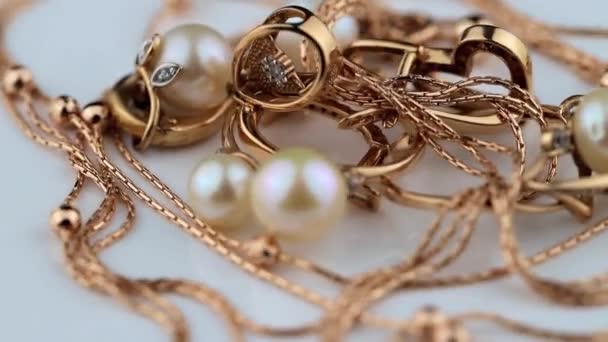 Χρυσά σκουλαρίκια και δαχτυλίδια με πολύτιμους λίθους και μαργαριτάρια περιστρέφονται σε λευκή επιφάνεια - Πλάνα, βίντεο