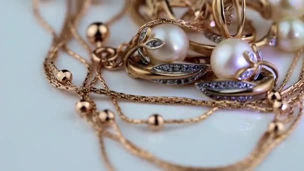 Fehér felületen arany fülbevalók és drágakövekkel és gyöngyökkel díszített gyűrűk forognak - Felvétel, videó