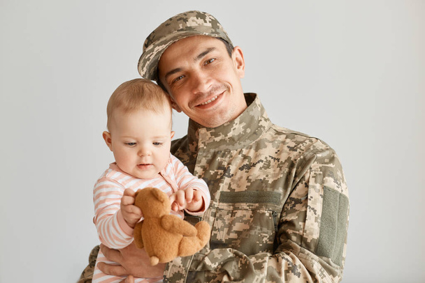Portrait of happy positive father came from the war or the army exercises and holding his charming baby, looks cute, expressing love, missing his family during military serve. - Photo, Image