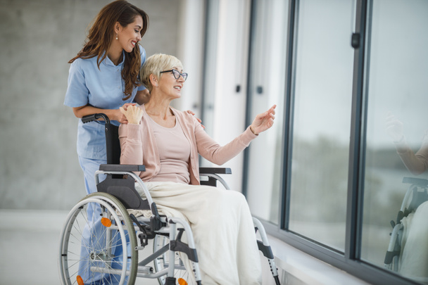 Prise de vue d'une jeune infirmière soignant une patiente âgée en fauteuil roulant. - Photo, image