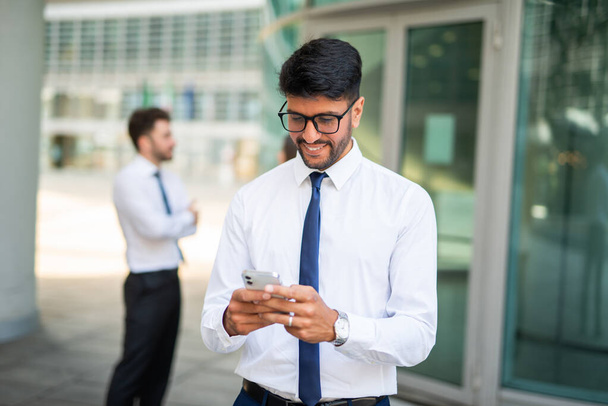 Hombre de negocios sonriente usando su teléfono celular frente a un grupo de colegas, concepto de trabajo en equipo - Foto, imagen
