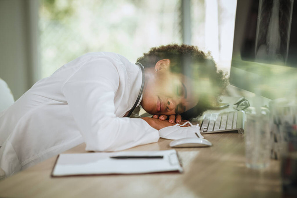 Colpo di una dottoressa africana stanca sdraiata sulle braccia incrociate alla scrivania mentre guardava i raggi X sul computer durante la pandemia del COVID-19. - Foto, immagini