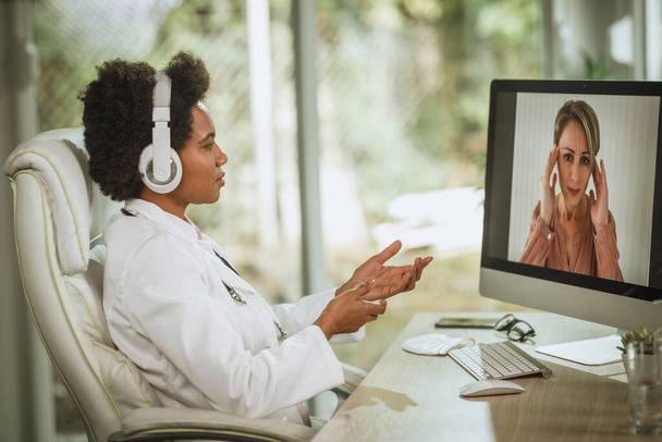 Foto di una dottoressa africana in videochiamata con paziente al computer nella sua stanza di consulenza durante la pandemia del COVID-19. - Foto, immagini