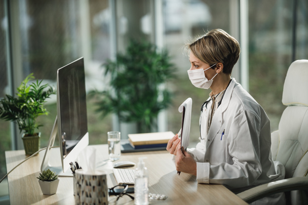 Во время пандемии COVID-19 женщина-врач в защитной маске проводит видеозвонок с пациентом на компьютере. - Фото, изображение