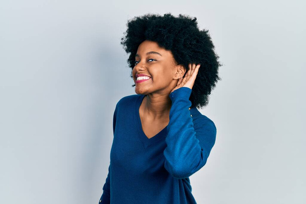 Νεαρή Αφροαμερικάνα που φοράει καθημερινά ρούχα χαμογελώντας αφουγκραζόμενη και ακούγοντας φήμες ή κουτσομπολιά. έννοια της κώφωσης.  - Φωτογραφία, εικόνα
