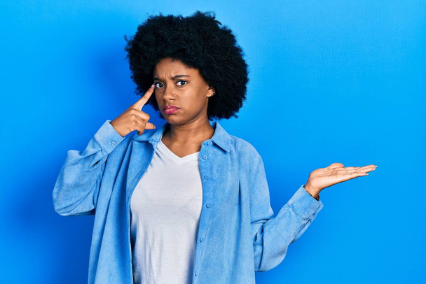 Jovem afro-americana vestindo roupas casuais confusa e irritada com palma aberta mostrando espaço de cópia e apontando o dedo para a testa. Pense nisso..  - Foto, Imagem