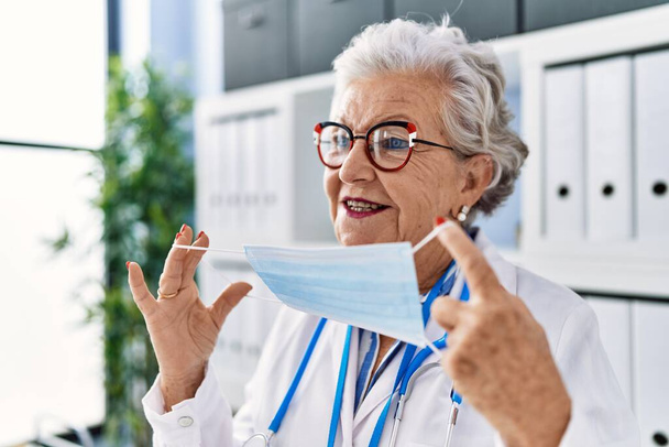 Starsza siwowłosa kobieta w mundurze lekarza i masce medycznej w klinice - Zdjęcie, obraz