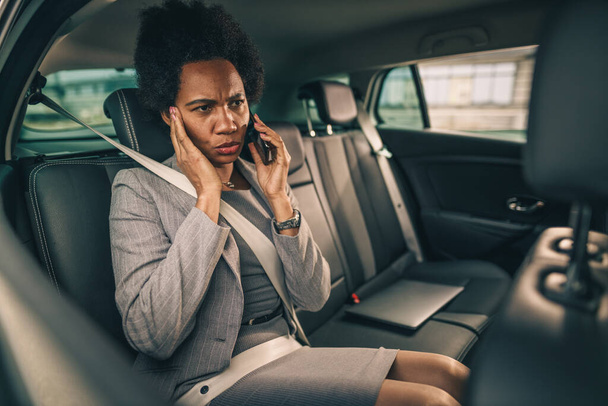 Shot of a successful black woman talking on a smartphone while sitting in the backseat of a car during her business commute. - Photo, Image