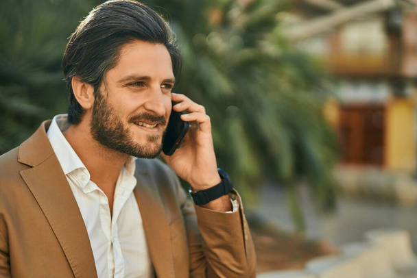 Молодой латиноамериканец-бизнесмен улыбается счастливо разговаривая на смартфоне в городе. - Фото, изображение
