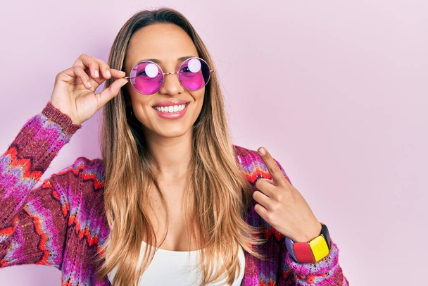 Mooie Spaanse vrouw in bohemien en hippie stijl met roze zonnebril lachend vrolijk wijzend met hand en vinger  - Foto, afbeelding