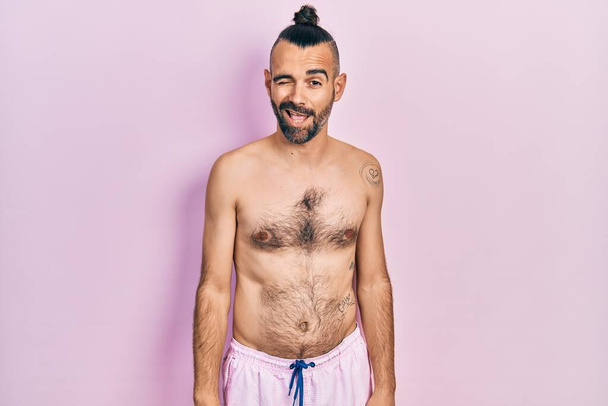 Молодий іспаномовний чоловік одягнений в купальник підморгує дивитися на камеру з сексуальним виразом, веселим і щасливим обличчям
.  - Фото, зображення