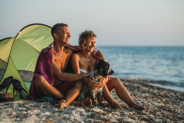 Una joven pareja cariñosa pasando el día en la playa con su lindo perro Cocker Spaniel. - Foto, imagen