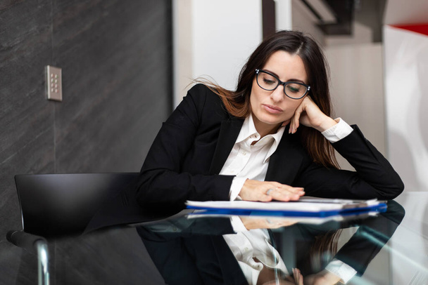 Молодая женщина-менеджер сидит за своим столом в современном офисе и выглядит скучно - Фото, изображение