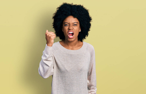 Young african american woman wearing casual clothes angry and mad raising fist frustrated and furious while shouting with anger. rage and aggressive concept.  - Photo, Image