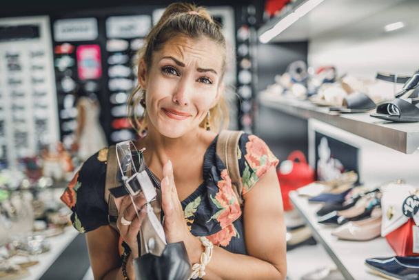 Atrakcyjna kobieta z żebraczymi dłońmi prosząc męża kupić eleganckie buty, ciesząc się dniem w centrum handlowym. - Zdjęcie, obraz