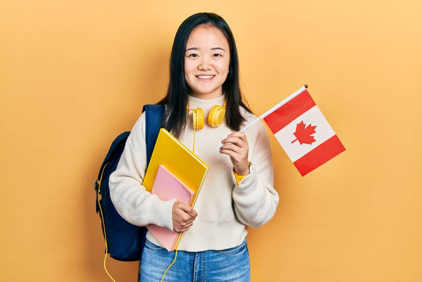 Giovane studentessa cinese scambio tenendo bandiera del Canada sorridente con un sorriso felice e fresco sul viso. mostrando i denti.  - Foto, immagini