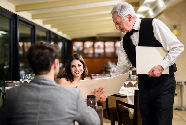 Waiter giving a menu to a couple in an elegant restaurant - Foto, afbeelding