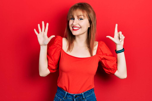 Redhead young woman wearing casual red t shirt showing and pointing up with fingers number seven while smiling confident and happy.  - Foto, immagini