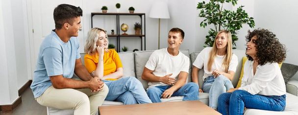 Groupe de jeunes amis souriant heureux assis sur le canapé à la maison. - Photo, image