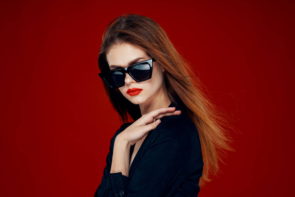 cheerful fashionable woman wearing sunglasses red lips posing red background - Foto, immagini