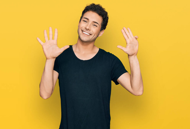 Young handsome man wearing casual black t shirt showing and pointing up with fingers number nine while smiling confident and happy.  - Zdjęcie, obraz