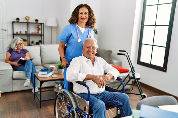 Médico de mediana edad mujer apoyando a un hombre jubilado sentado en silla de ruedas en un hogar de ancianos. - Foto, imagen