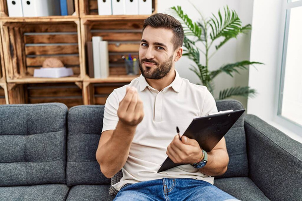 Handsome hispanic man holding clipboard working at psychology clinic doing money gesture with hands, asking for salary payment, millionaire business  - Photo, image
