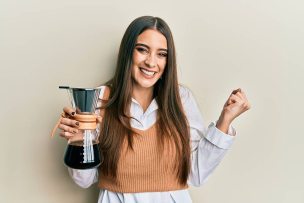 Güzel esmer kadın, elinde çözünebilir kahve makinesiyle gururla bağırıyor zaferi ve başarıyı kutluyor.  - Fotoğraf, Görsel