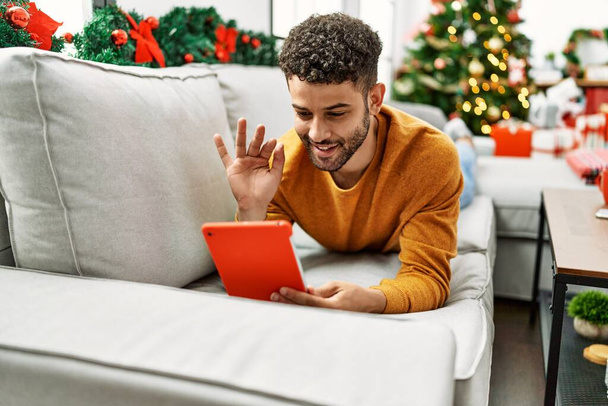 Young arab man having video call lying on the sofa by christmas tree at home. - Photo, image