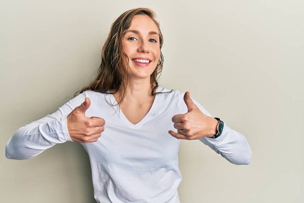 Young blonde woman wearing casual clothes success sign doing positive gesture with hand, thumbs up smiling and happy. cheerful expression and winner gesture.  - Foto, afbeelding