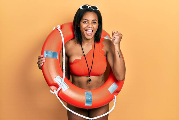 Young african american girl wearing bikini and holding lifeguard float screaming proud, celebrating victory and success very excited with raised arms  - Foto, Bild