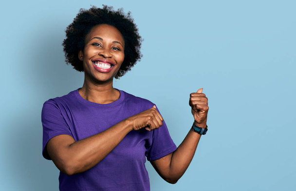 Africká americká žena s afro vlasy na sobě ležérní fialové tričko ukazuje na zadní straně s rukou a palci nahoru, s úsměvem sebevědomě  - Fotografie, Obrázek