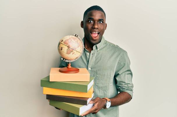 Young african american man holding vintage world ball and books celebrating crazy and amazed for success with open eyes screaming excited.  - Foto, Imagem