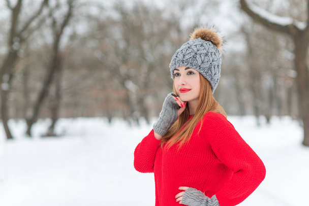 Красивая молодая девушка в красном пальто зимняя рождественская одежда, и шерстяная шапка на фоне природы. Солнечный портрет модной дамы - Фото, изображение