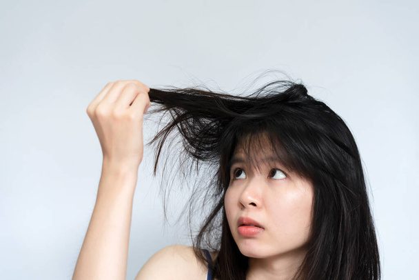 Una mujer mira la mano sosteniendo su propio cabello dañado y desordenado. - Foto, Imagen