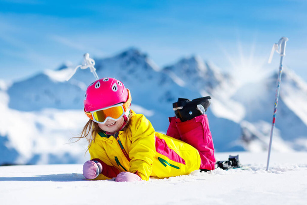 Çocuk dağlarda kayak yapıyor. Güvenlik kaskı, gözlüğü ve direkleri olan aktif bir çocuk. Küçük çocuklar için kayak yarışı. Aile için kış sporu. Alp okulunda çocuklar kayak dersi alıyor. Küçük kayakçı karda yarışıyor - Fotoğraf, Görsel