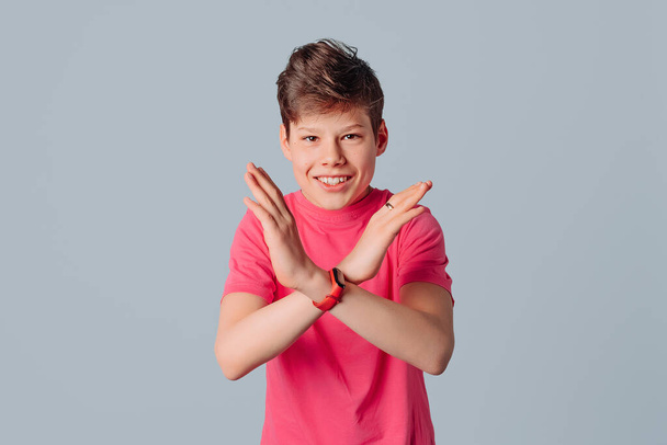 Retrato de adolescente em camiseta rosa casual, mostrando discordância ao fazer x gesto de mão cruzada, de pé sobre fundo cinza - Foto, Imagem