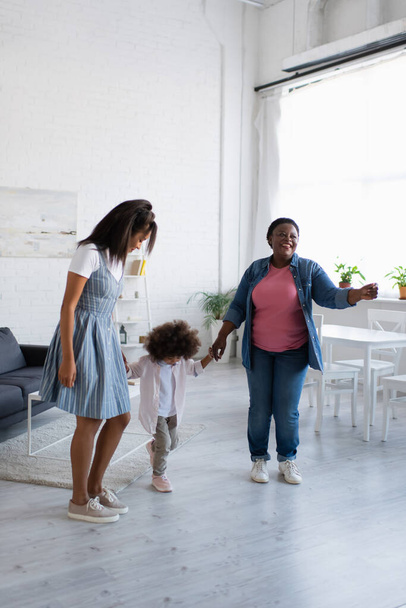 cheerful african american women holding hands and dancing with toddler girl at home - Foto, immagini