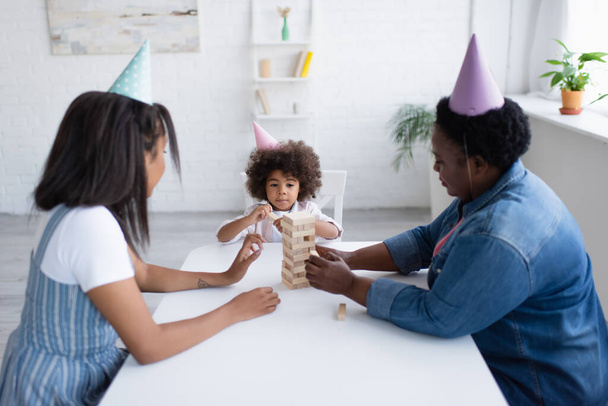 パーティーキャップでアフリカ系アメリカ人女性と子供が自宅で木のブロックゲームをプレイ - 写真・画像