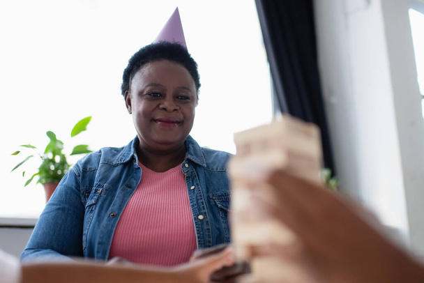 щаслива афроамериканська жінка середнього віку, дивлячись на розмиту сім'ю, граючи в дерев'яні блоки
 - Фото, зображення