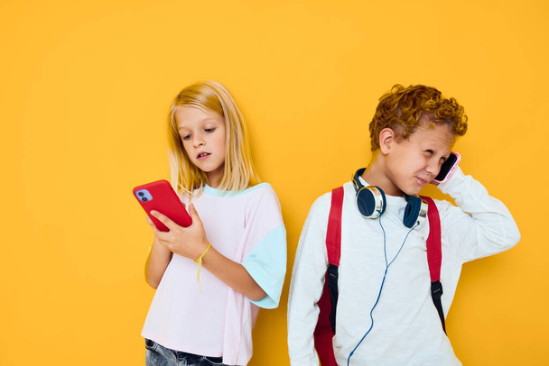 Two kids boy and girl looking at the phone entertainment communication yellow background - Foto, afbeelding
